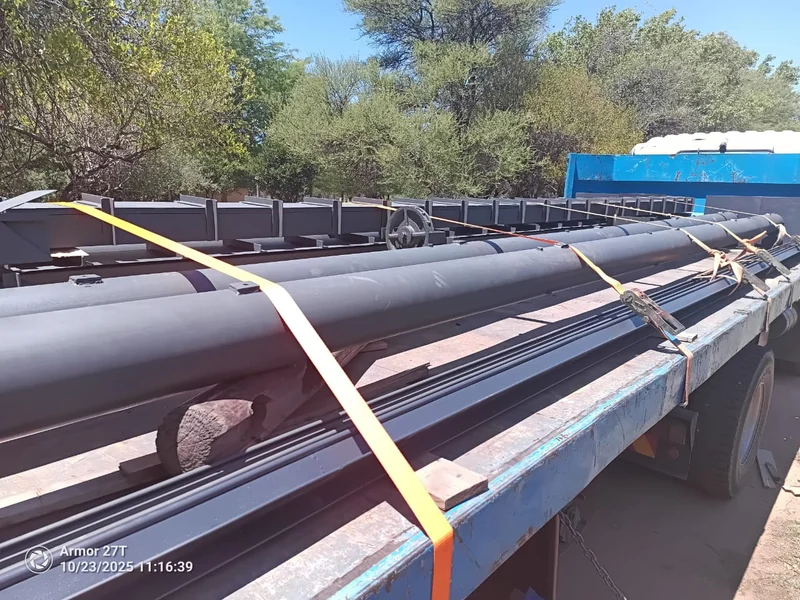 Shafts and guide rails, strapped: Barrel shafts and steel guide rails ratchet-strapped on a flatbed — every component of the door travels as one load.