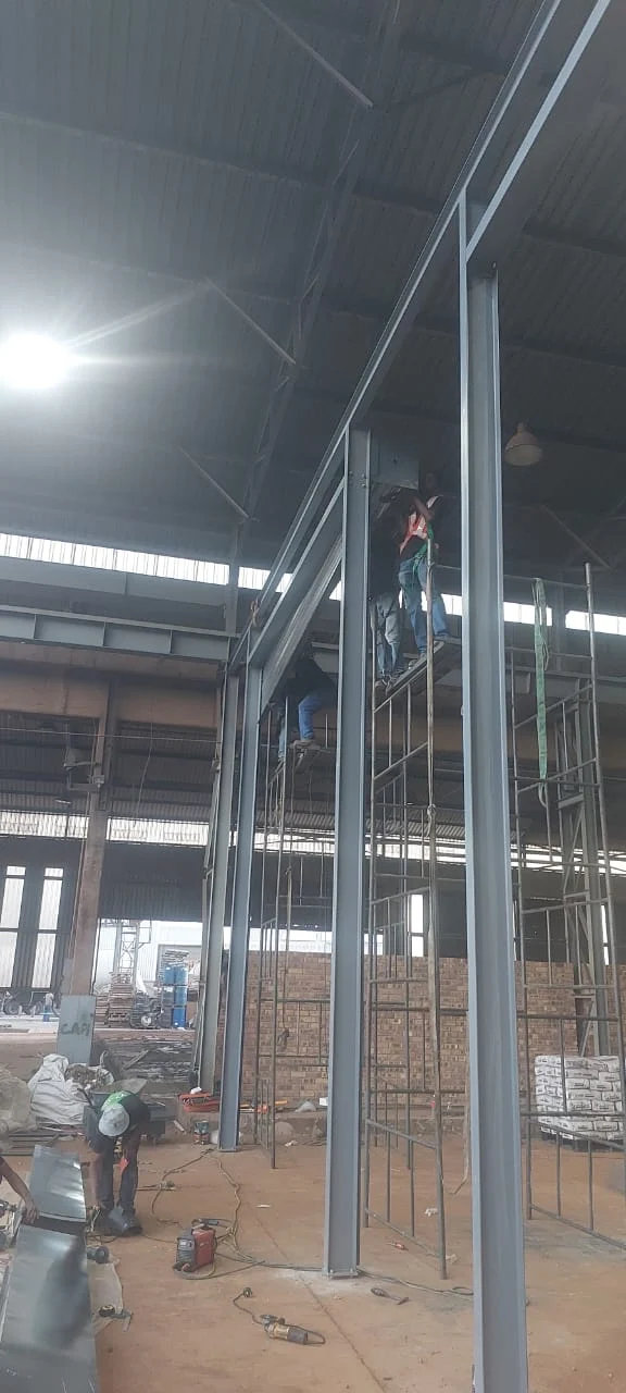 Frame erection at height: Our crew erecting tall steel columns and beams from scaffolding inside an industrial building.